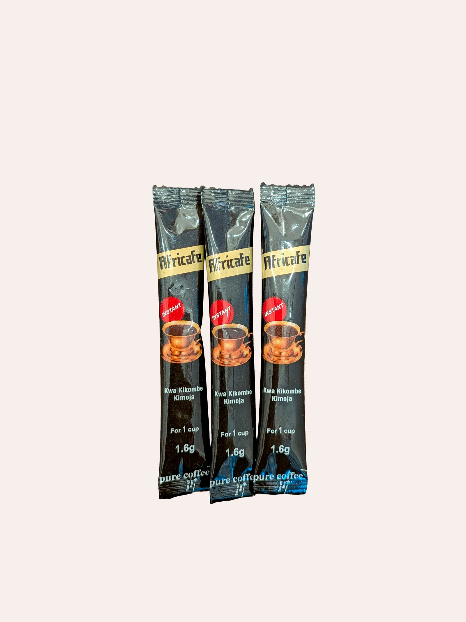 Africafe instant coffee single-serve sticks — three black and gold 1.6g stick sachets fanned out, each with a red 'Instant' mark, a cup of coffee, 'Kwa Kikombe Kimoja / For 1 cup', and a 'pure coffee' band